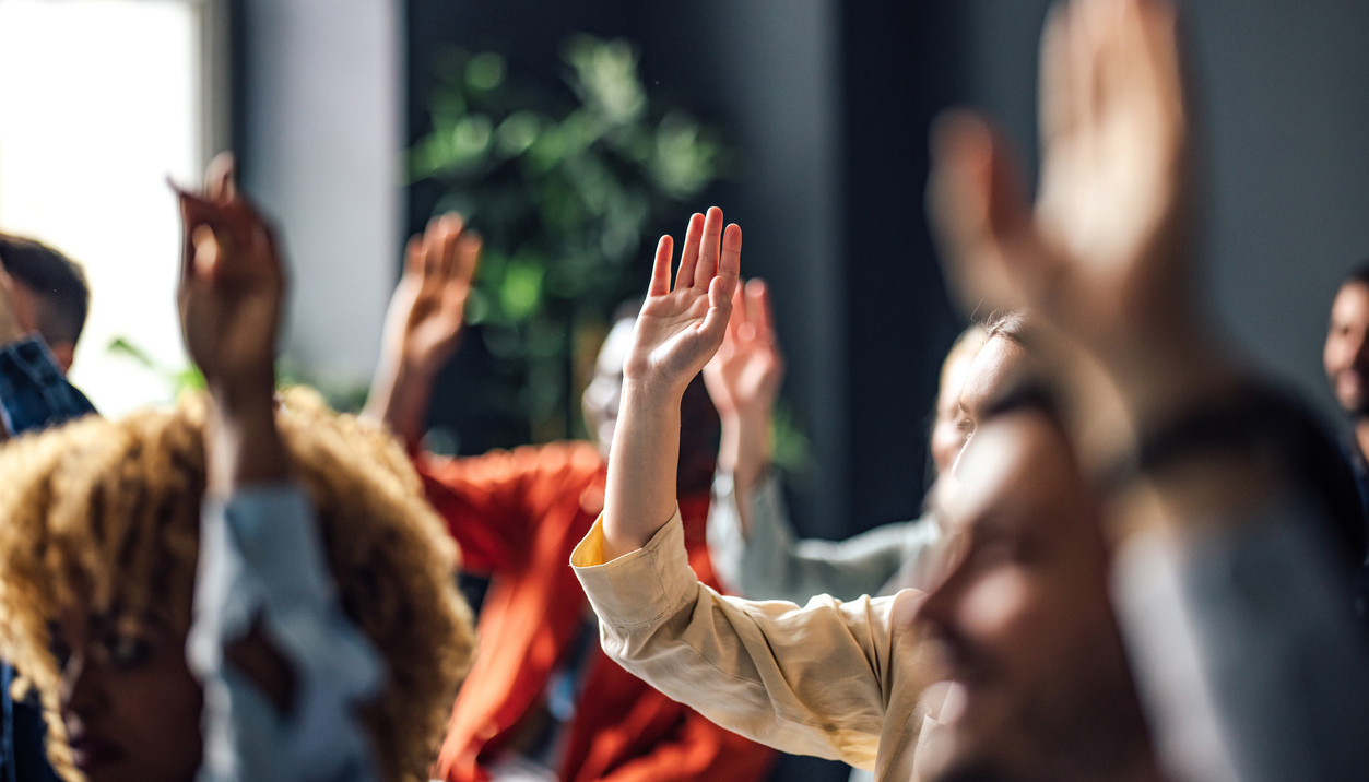 Group of people sitting on a seminar. They have their hand raised.