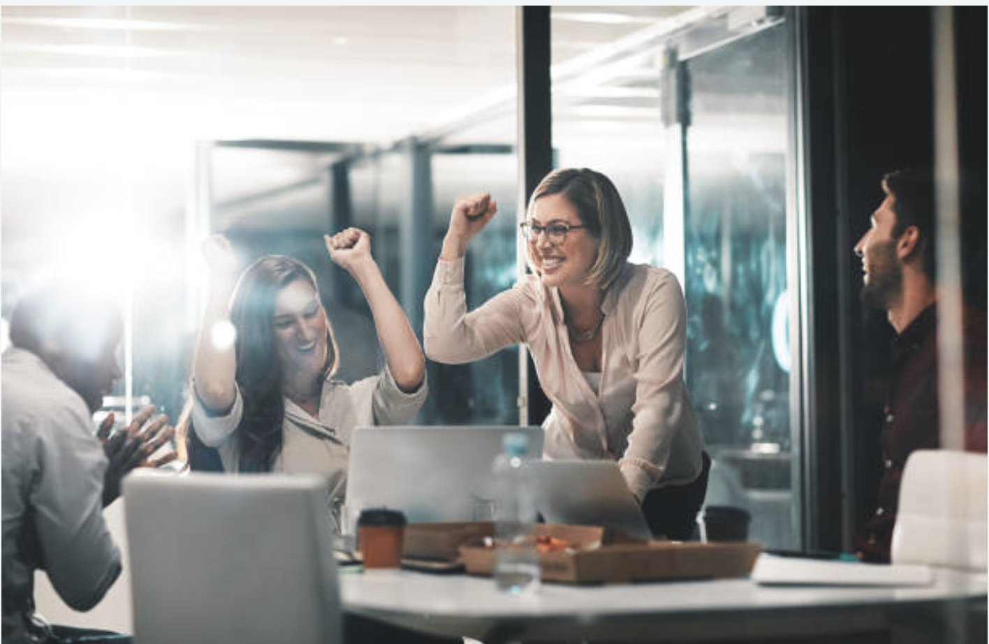 Group of professionals smiling and raising their hands in celebration in a corporate board room. 